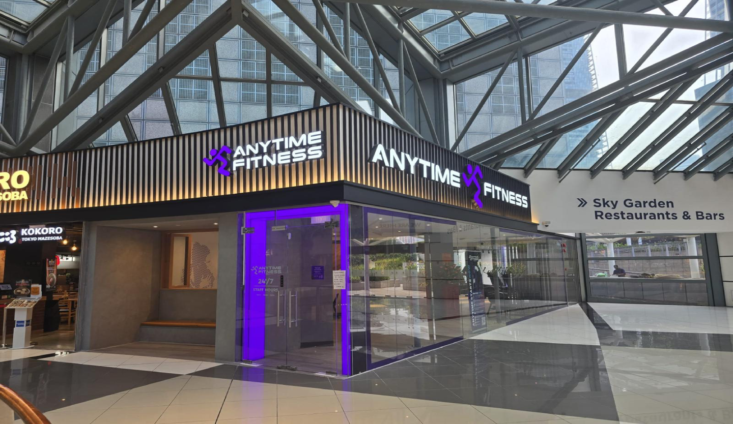 Anytime Fitness gym storefront fit-out by Trident Fitout, corner unit beneath a steel-framed glass atrium next to Sky Garden Restaurants and Bars