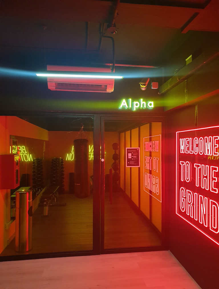 Alpha training room fit-out by Trident Fitout, boxing bag and weights area beneath red neon Welcome To The Grind signage