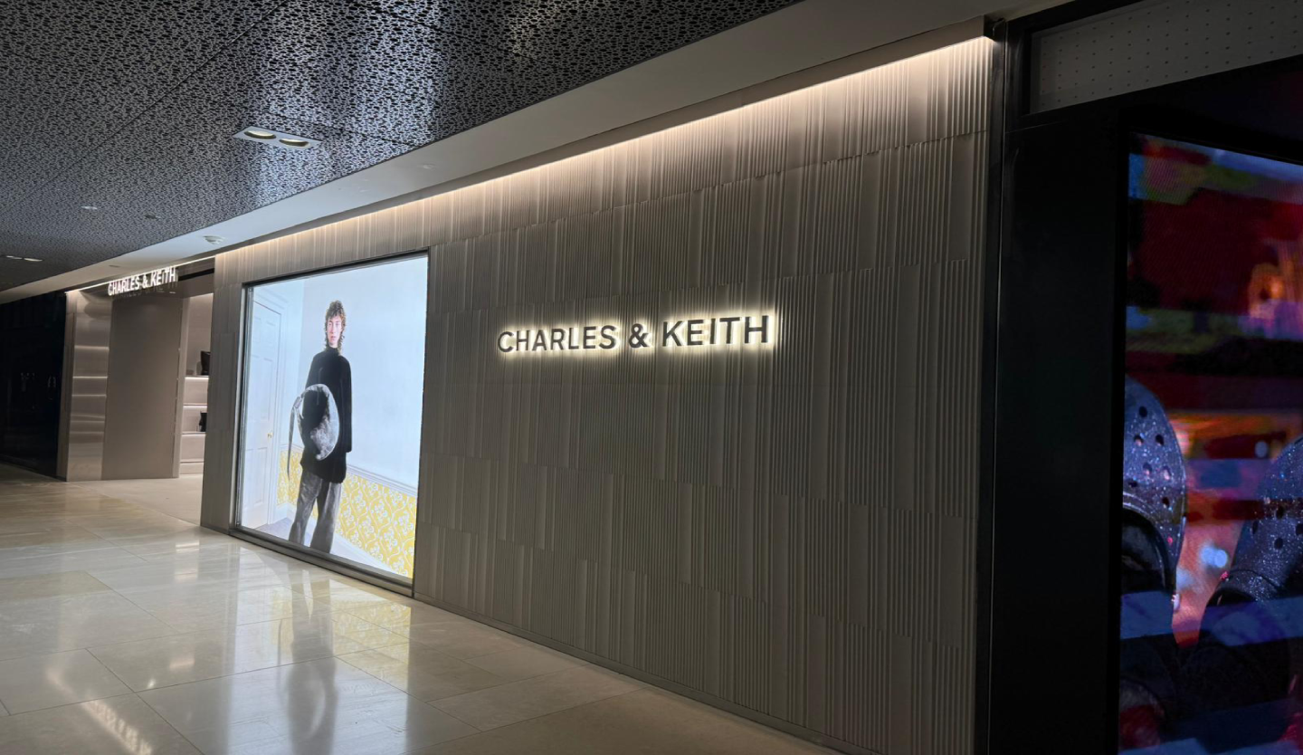 Charles & Keith retail store fit-out by Trident Fitout, backlit wordmark signage beside a lookbook display screen