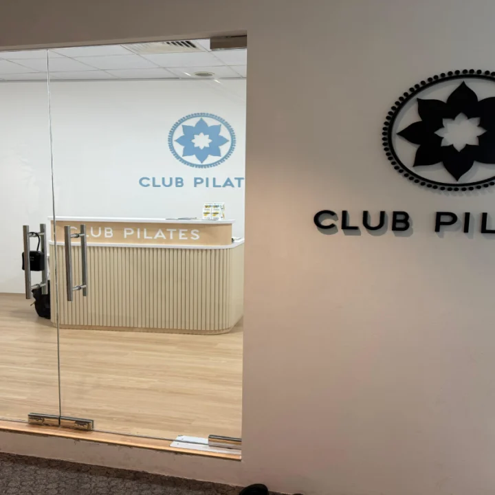 Club Pilates studio entrance fit-out by Trident Fitout, glass door beside the reception counter and a retail rack of branded apparel
