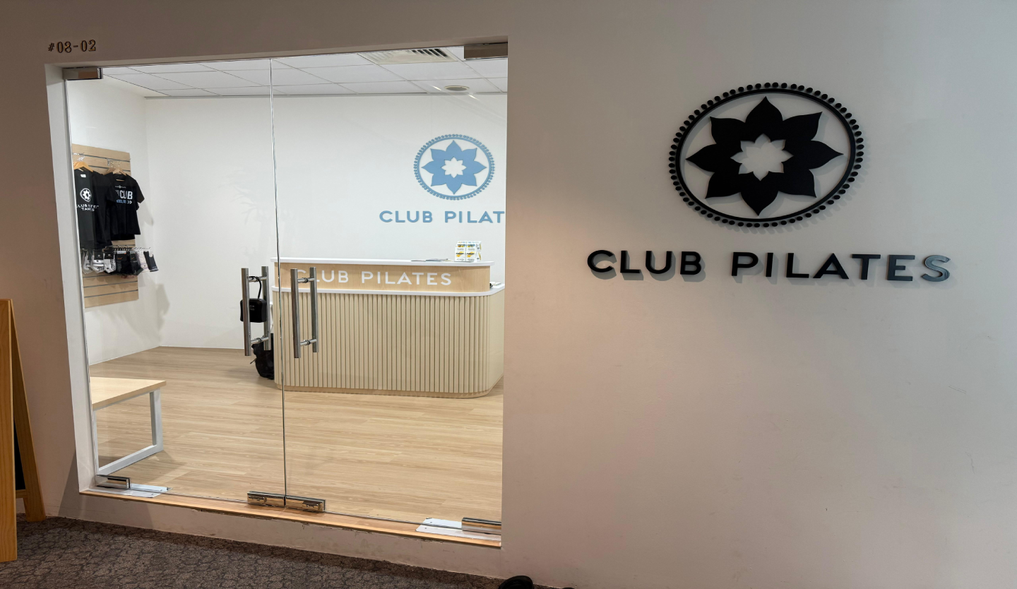 Club Pilates studio entrance fit-out by Trident Fitout, glass door beside the reception counter and a retail rack of branded apparel
