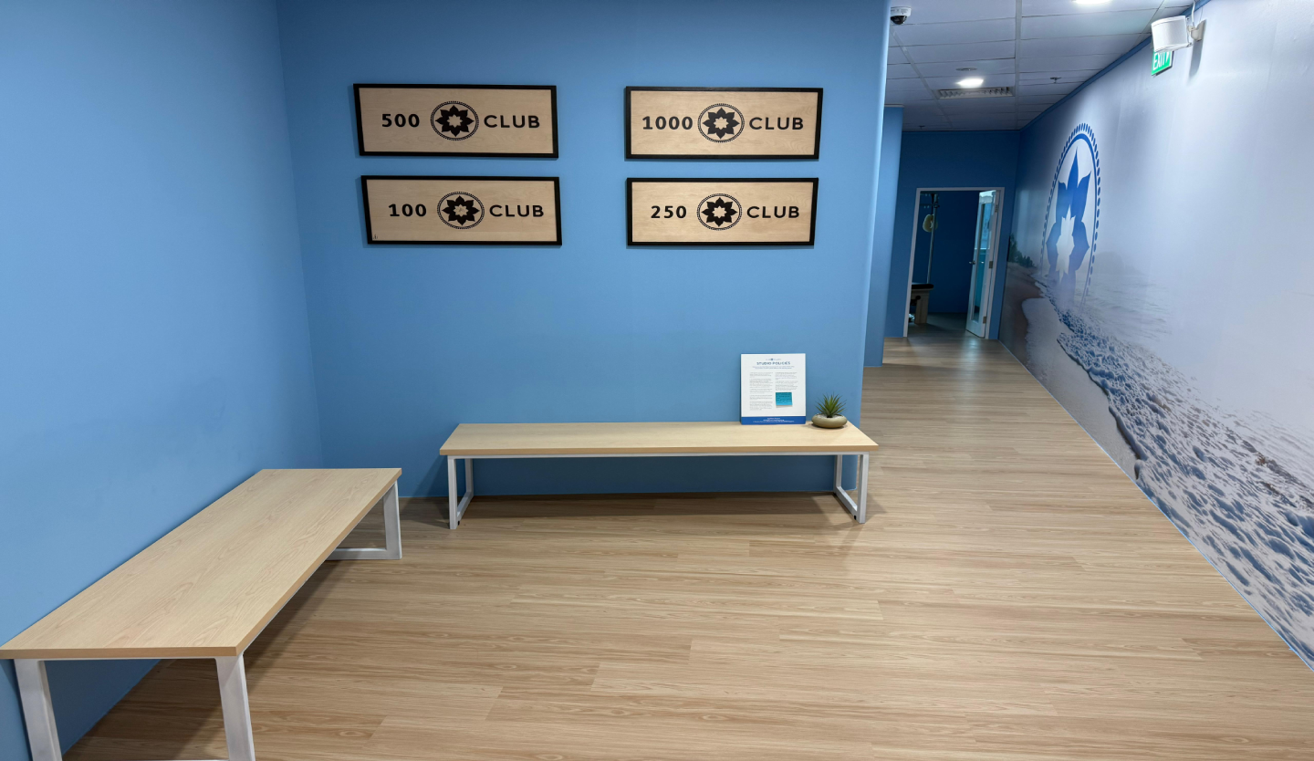 Club Pilates studio corridor fit-out by Trident Fitout, milestone club plaques on a blue feature wall leading to an ocean mural corridor