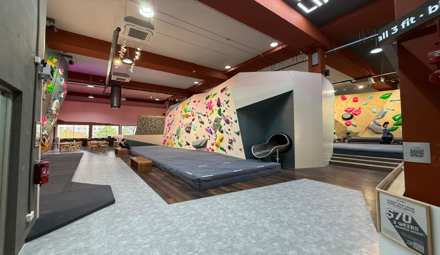 Fitbloc bouldering gym fit-out by Trident Fitout, colour-coded climbing walls and crash mats with the cafe seating area visible beyond