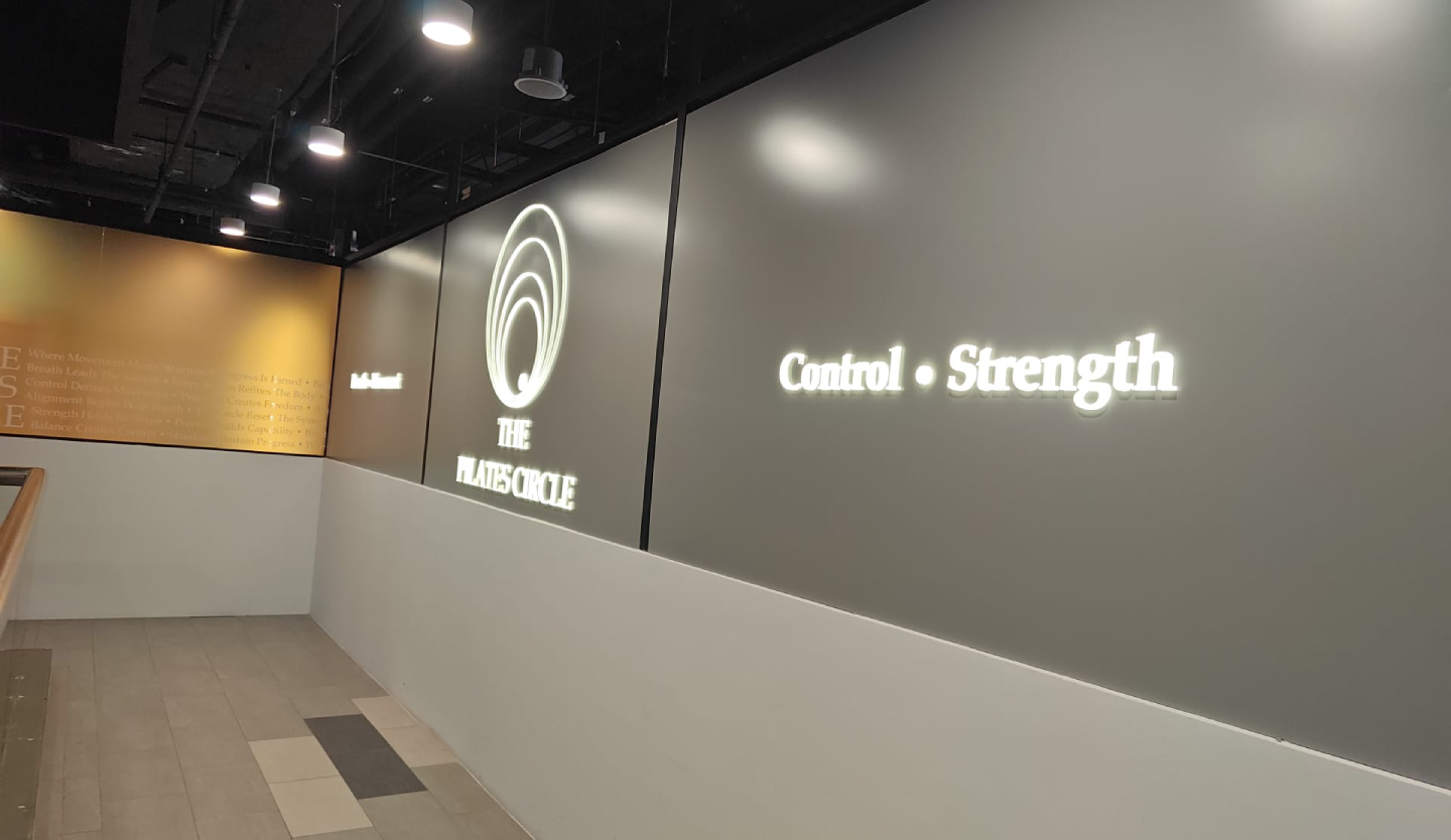 Illuminated wall signage inside The Pilates Circle studio reading "Control • Strength" beside the brand's circular logo, with a mission statement in gold text visible on the wall to the left.